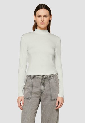 Un turtleneck blanc à manches longues en tissu doux, présentant un design ajusté et un col haut. Associé à un jean léger gris clair taille haute avec des coutures bien marquées.