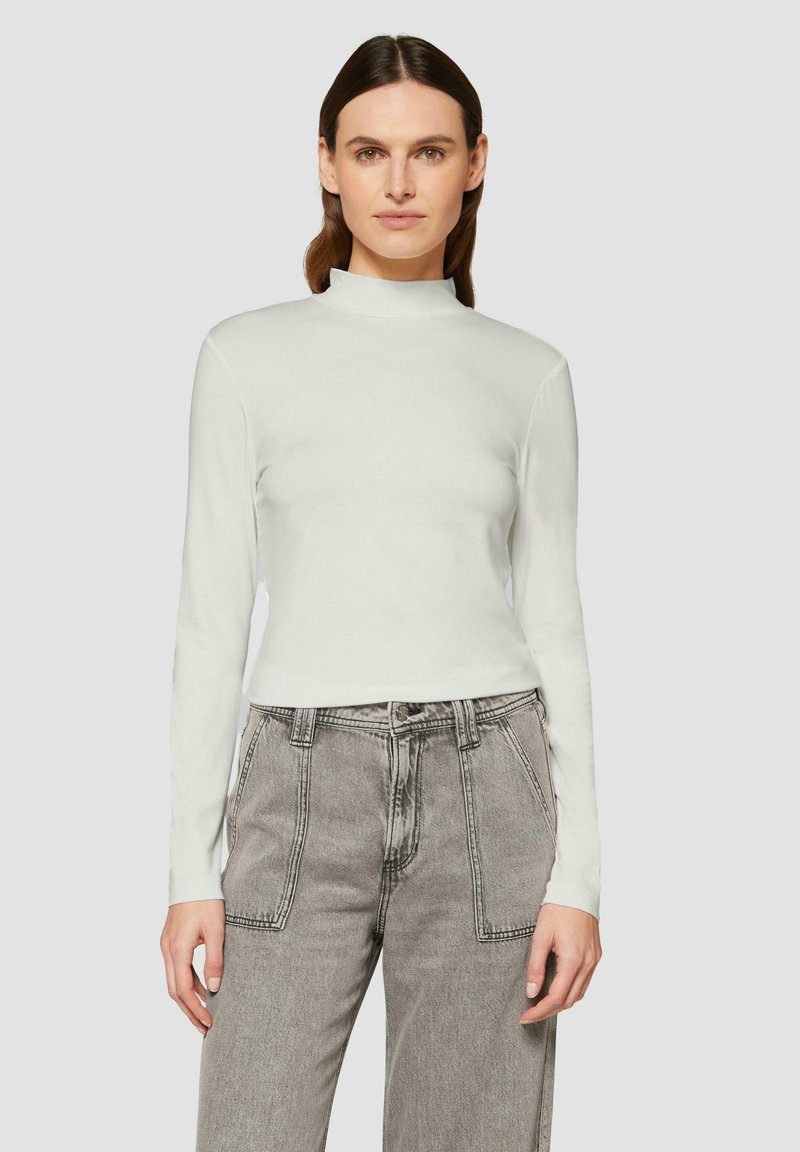 Un turtleneck blanc à manches longues en tissu doux, présentant un design ajusté et un col haut. Associé à un jean léger gris clair taille haute avec des coutures bien marquées.