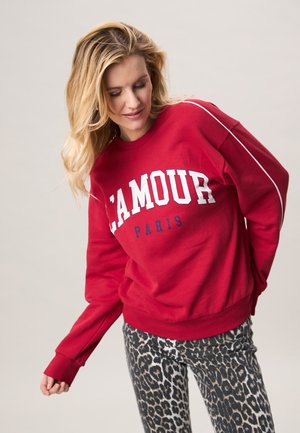 Rode sweatstoftrui met witte letters "L'AMOUR PARIS", ontspannen pasvorm, geribbelde manchetten, gecombineerd met zwarte en grijze legging met dierenprint.