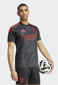 Juoda trumpa rankovėmis futbolo marškinėliai su raudonais akcentais, pasižymintys žvaigždžių raštu ir "Emirates Fly Better" logotipu; derinami su juodomis šortais.