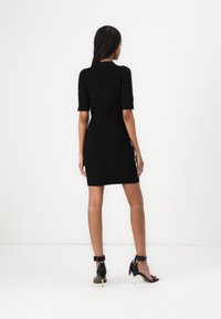 Μαύρο πλεκτό φόρεμα, εφαρμοστή σχεδίαση, κοντά μανίκια, μέχρι το γόνατο. Συνδυασμένο με μαύρα πέδιλα με λουράκια που περιβάλλουν τον αστράγαλο και διακοσμητικά στοιχεία.