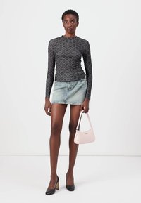 Long-sleeve black top with geometric pattern, paired with a light denim skirt. Holding a small light pink handbag. Black high-heeled shoes.