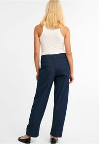 Hochtaillierte, dunkelblaue, weite Jeanshose mit Gesäßtaschen, kombiniert mit einem enganliegenden, gerippten weißen Tanktop und schwarzen Ballerinas.