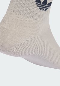 Calcetín deportivo beige con tejido texturizado, que presenta un logo y rayas en azul oscuro. Acabado liso y ajuste ceñido alrededor del tobillo.