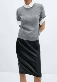 Grauer Pullover mit hochgerollten Ärmeln über einem schwarzen Leder-Bleistiftrock, der glatte Texturen und eine schlanke Silhouette präsentiert.