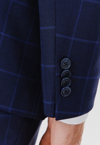 Marynarko-granatowy rękaw żakietu w delikatny wzór w kratkę, z czterema ciemnymi guzikami i gładką teksturą. Elegancki i dopasowany design.