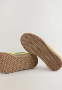 Schuh mit einem gelben und blauen Obermaterial, strukturiertem Gummisohle und einem geometrischen Muster an der Unterseite. Verfügt über ein niedriges Profildesign.