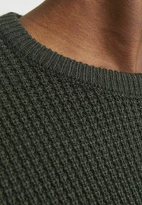 Maglione lavorato a maglia verde scuro con un colletto a coste testurizzato e una vista ravvicinata dell'intricato motivo del tessuto.