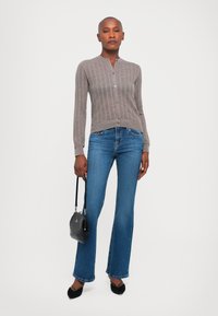 Svetlošedý pletený kardigán s rebrovanou textúrou, so zapínaním na gombíky, v kombinácii s rozšírenými modrými džínsami a malou čiernou textúrovanou kabelkou.