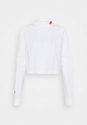 White cropped long-sleeve turtleneck made of cotton. Features a small red flame logo on the collar and red accents on the sleeve cuffs.