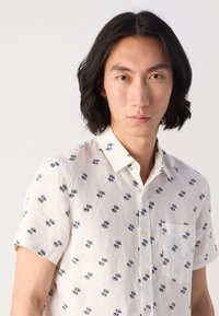 Short-sleeve shirt in a lightweight, cream fabric featuring a navy-blue geometric pattern, with a button-down collar and front pocket.