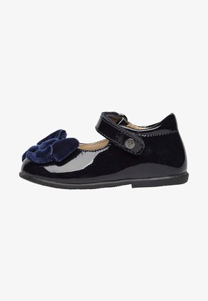 Scarpa Mary Jane in patent e velluto nero con un grande dettaglio a fiocco, fissata da una tracolla regolabile e una suola in gomma piatta.