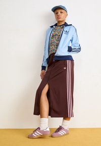 Ljusblå zip-jacka med marinblå detaljer, blommig skjorta, brun kjol med rosa ränder, och lila träningsskor med vita ränder.