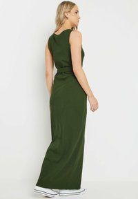 Robe maxi verte à côtes avec un corsage ajusté, de larges bretelles et un détail de lien sur le côté. Associée à des baskets blanches.