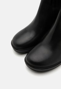 Botines negros de tobillo con un acabado de cuero suave, puntera redondeada y una sutil textura mate. Presentan una suela baja y robusta para mayor comodidad.