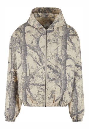 Tuunika kapuutsiga, helebeeži värvusega ja halli puuoksi mustriga, esilukuga ja elastsete varrukaääreosadega, mis tagavad tiheda lõike.