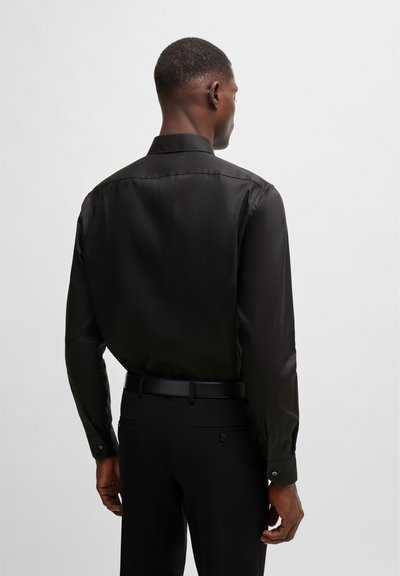 Chemise noire à manches longues en tissu doux, avec un col classique, des poignets à boutons et une coupe ajustée, assortie à un pantalon noir.