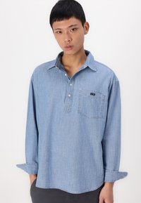 Cămașă din denim cu mânecă lungă, de culoare albastru deschis, având guler cu nasturi, buzunar cu logo-ul „GAP” și o croială relaxată cu manșete răsucite.
