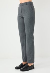 Grau gestreifte Hose mit taillierter Passform, ausgestattet mit einer glatten Stofftextur und einem klassischen Bund. Kombiniert mit schwarzen Slippern.