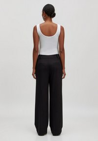 Witte geribbelde tanktop met een brede ronde rug, gecombineerd met hoge, zwarte, wijde broeken met zijzakken en geplooide details.