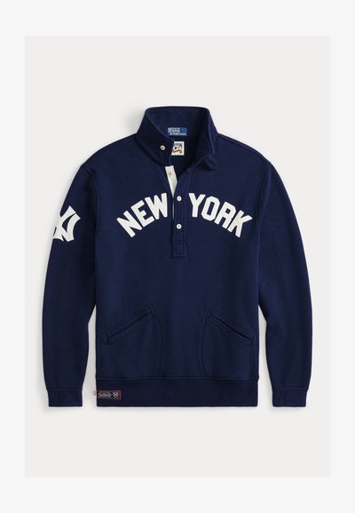 Tamsiai mėlynas megztinis su aukštu apykakle, baltu "NEW YORK" užrašu ir dviem priekinėmis kišenėmis. Yra mažas logotipas ant apdailos.