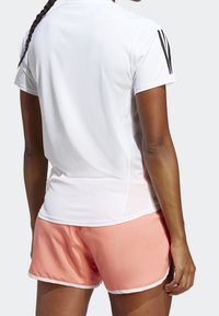 Vit sporttröja med svarta detaljer och korta ärmar, i kombination med rosa shorts med vit kant. Ventilerande mesh-sidopanel synlig.