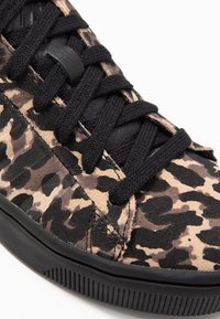 Tenisky s leopardím vzorem v béžové a hnědé semišové úpravě, s černými tkaničkami a strukturovanou černou gumovou podrážkou. Detailní záběr.