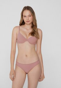 Formgepresster BH und passender Bikini aus weichem, staubigem Pink. Glatte Textur mit dünnen Trägern und minimalistischer Gestaltung.
