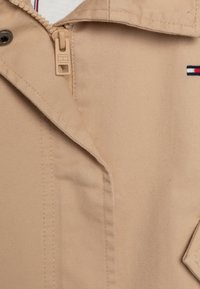 Giacca beige in tessuto testurizzato, con zip e colletto a revers. Comprende un piccolo dettaglio del logo con accenti rossi, bianchi e blu.