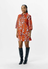 Vestido de patrón floral rojo con cuello y mangas cortas, que presenta diseños de hojas azules, combinado con botas altas negras.