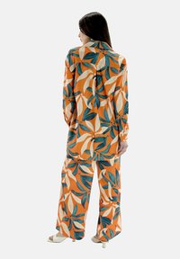 Oranje patroonoutfit met grote bladeren in groen en crème. Het ontwerp beslaat zowel een losse top als wijde broek.