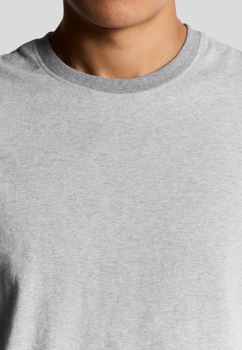 Camiseta gris claro hecha de un material suave con un cuello redondo y un ribete gris en contraste. Presenta una textura suave y un diseño minimalista.