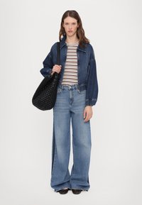 Denim jacket, striped cotton top, and wide-leg jeans in light blue. Black woven bag. Features casual design and relaxed fit.