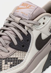 Scarpa Nike Air Max in beige e grigio. Presenta pelle testurizzata, dettagli con motivo e una linguetta imbottita con marchio. Chiusura con lacci.