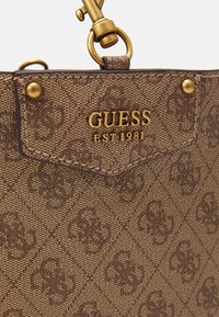 Borsa a mano marrone con motivo, con logo impresso, hardware dorato e dettagli tattili; presenta un attacco per tracolla e branding.