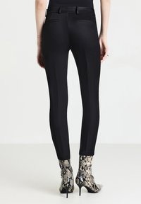 Femme portant un pantalon noir ajusté avec des poches arrière et des bottines à talons aiguilles en motif peau de serpent.