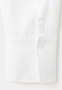 Weißer Hemdärmel mit Manschette, die eine einzelne klare Knopföffnung und sichtbare Nahtdetails auf einem weichen Stoffhintergrund zeigt.