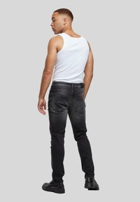Musta denimi housut, joissa on kulutettu pinta, slim fit -malli ja viisi taskua. Yhdistetty valkoiseen topiin ja mustiin kenkiin, nähty takaa.