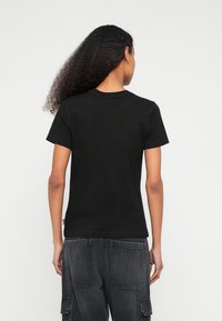 Čierne bavlnené tričko s krátkymi rukávmi a okrúhlym výstrihom, s hladkou textúrou a jednoduchým dizajnom, zobrazené zozadu.