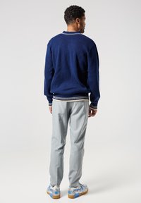 Námořnický úpletový svetr s bílým lemováním na límci a manžetách, kombinovaný se šedými pruhovanými kalhotami a teniskami s modrými akcenty.