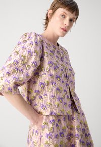 Brodert jakke i lavendel og grønn blomsterdesign, med puffermer og rund hals, laget av teksturert stoff.