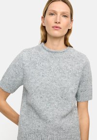 Szary sweter z krótkim rękawem wykonany z teksturowanego dzianinowego materiału, ozdobiony wielokolorowymi plamkami i o okrągłym dekolcie.