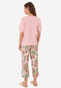 T-shirt rosa chiaro a maniche corte abbinato a pantaloni color pastello con una stampa botanica di piante e ananas. Tessuto morbido e vestibilità comoda.