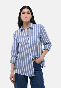 Chemise à manches longues rayée bleue et blanche avec une poche, en tissu léger ; possède des manches retroussées et une coupe ample.