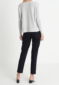 Hellgrauer strukturierter Pullover mit langen Ärmeln, kombiniert mit dunkelblauen maßgeschneiderten Hosen und weißen Blockabsatzschuhen, von hinten betrachtet.