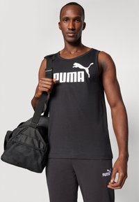 Svart ermeløs tanktop med hvit "PUMA"-logo, kombinert med svarte bukser og en svart treningsveske med nettseksjon og justerbar stropp.