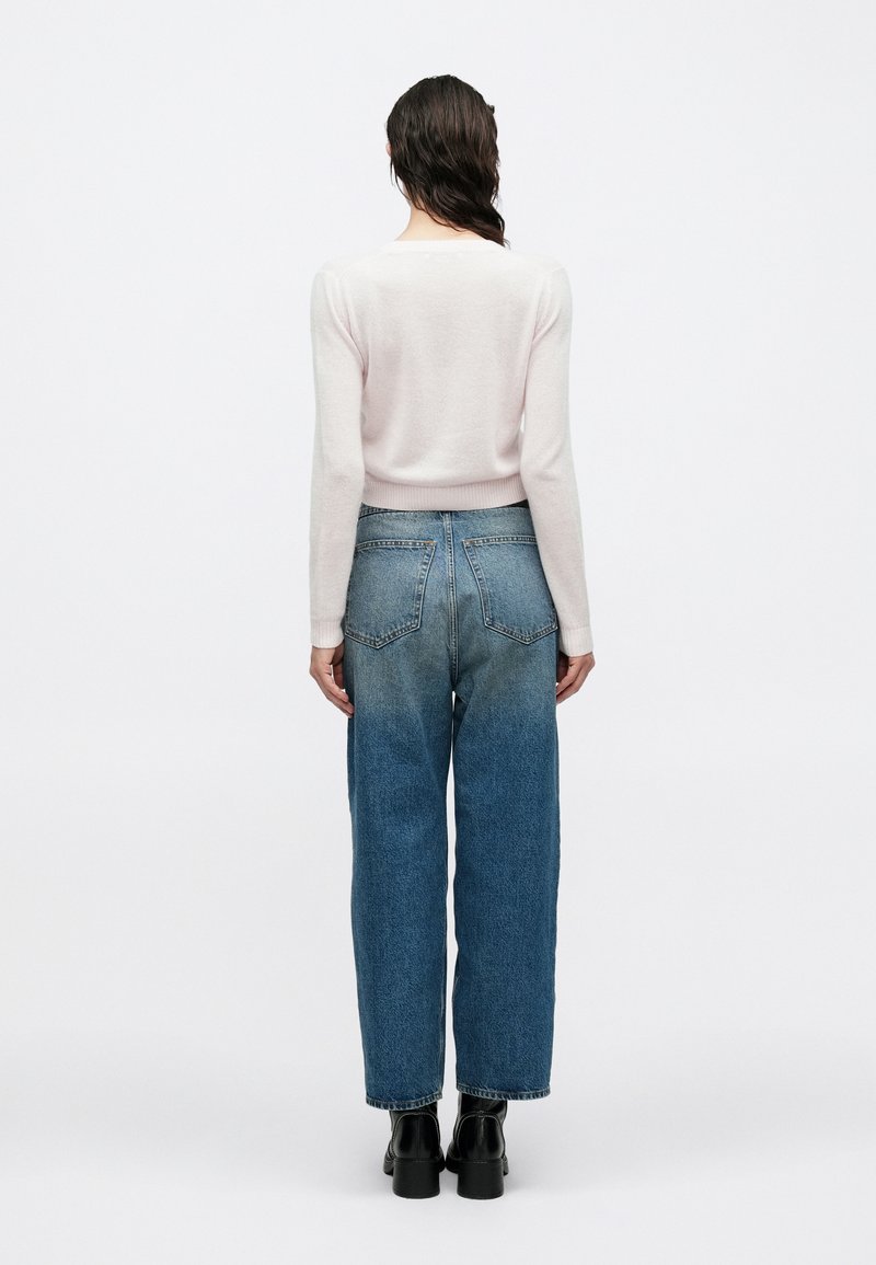 Hellrosa Pullover mit tailliertem Schnitt und geripptem Saum, kombiniert mit hoch taillierter blauer Jeans mit einem allmählichen Farbverlauf von hell nach dunkel.