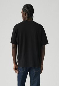 Black short-sleeve t-shirt made of cotton, featuring a relaxed fit and a straight hem. The back shows a smooth texture without embellishments.