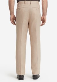 Beige linnedbukser med lige pasform, der har baglommer, en glat tekstur og subtile folder langs benene. Sorte sko er båret.