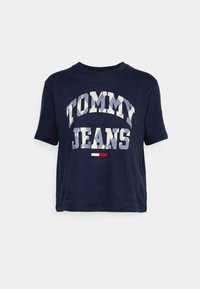 Námořnické tričko s krátkým rukávem vyrobené z bavlny, na kterém je text "TOMMY JEANS" v mozaikovém designu a malá trojbarevná značka pod ním.